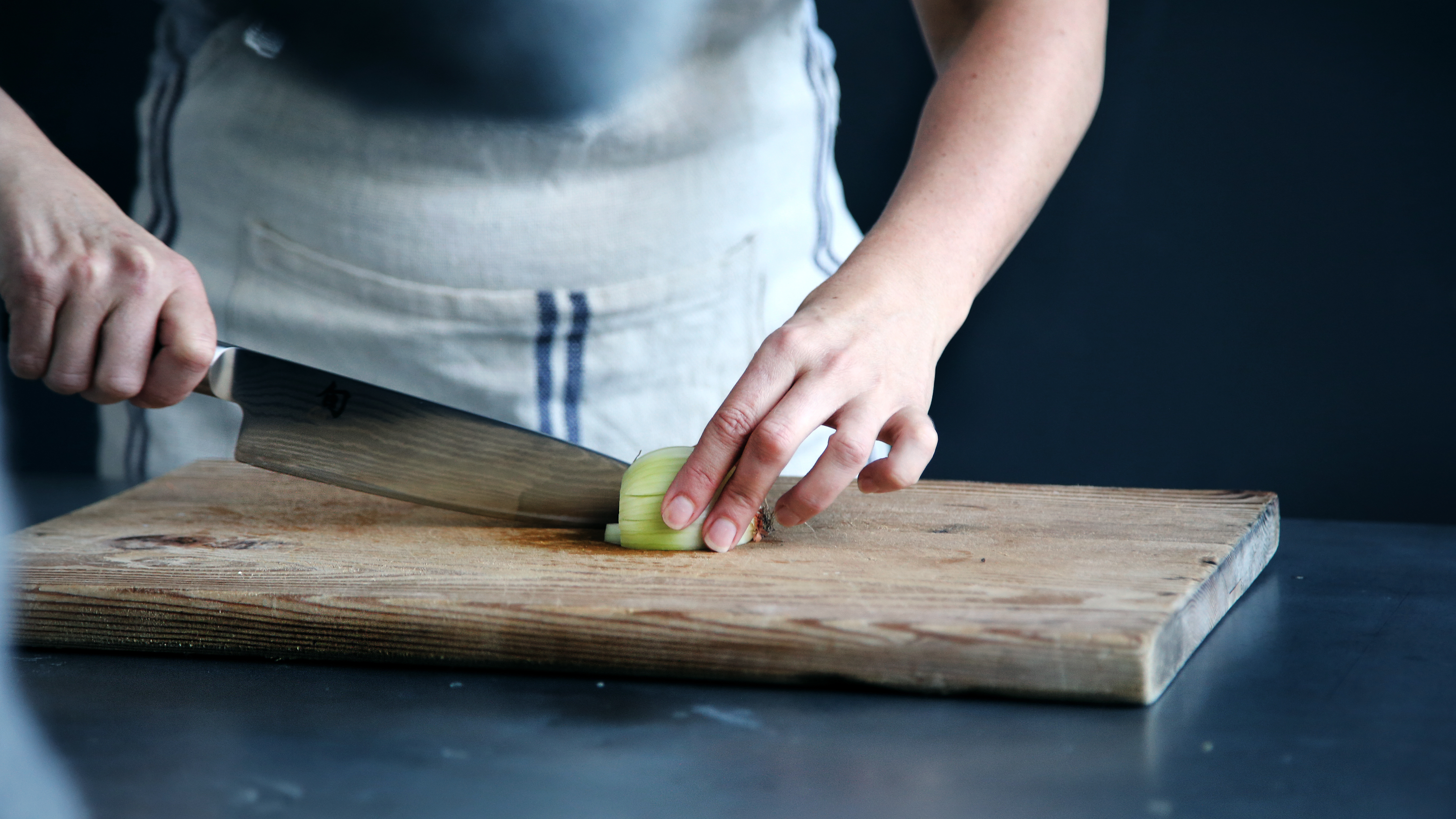 tutti i benefici della cucina e del cucinare - mani che tagliano cipolla con un grosso coltello da cucina, su un tagliere